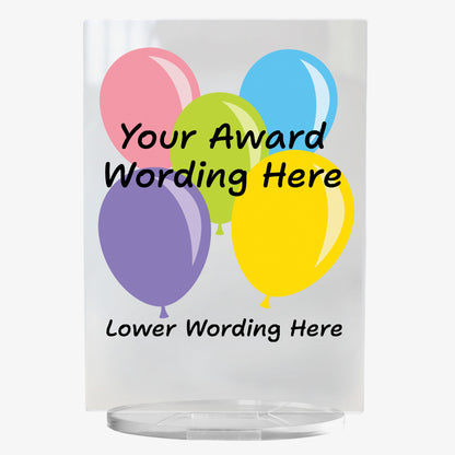 A clear acrylic award plaque standing on a circular base, featuring a selection of 5 colourful balloons - pink, green, blue, yellow and purple. Overlaying the balloons is placeholder text reading 'Your Award Wording Here' in bold black font. Below, additional text reads 'Lower Wording Here'. 