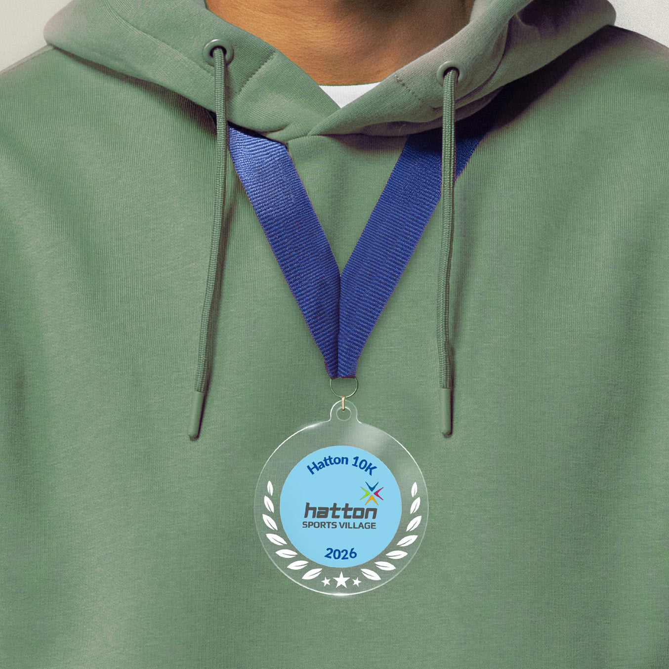 Acrylic personalised medal with blue ribbon showing wreath design with 'Hatton 10K 2026 wording', worn on a person in a green hoodie.