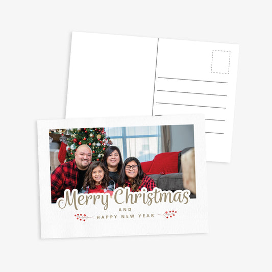Front and back of a festive Christmas postcard. The front features the text 'Merry Christmas and Happy New Year' and space to upload own photo - the image shows a family in front of a christmas tree. The back includes standard postcard lines for address and message