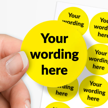 Hand holding a yellow circular sticker with 'Your wording here' text, surrounded by similar stickers.