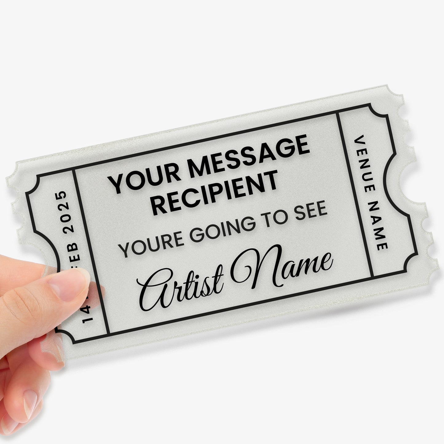A hand holding a custom acrylic gift ticket styled like an event pass, with decorative notched edges and a black border. The placeholder text reads: 'YOUR MESSAGE RECIPIENT – You're going to see... Artist name'. The left side shows the date '14 FEB 2025', and the right side has a placeholder reading 'VENUE NAME'. The design mimics a theatre or concert ticket, making it a fun and memorable birthday gift.