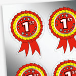 Sheet of rosette reward stickers.  The main rosette is red with a yellow inner ruffle.  The centre of the rosette is red with a large '1st' in white font central to the design with 5 metallic silver stars enclicling the '1st' above and below.