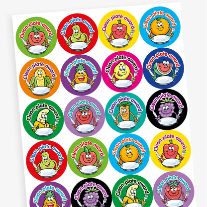 A sheet of colourful circular 'Clean Plate Award' stickers featuring smiling cartoon fruits and vegetables, such as an apple, pear, corn, and pineapple, each holding a knife and fork with an empty plate. Background colours include green, red, orange, and purple.