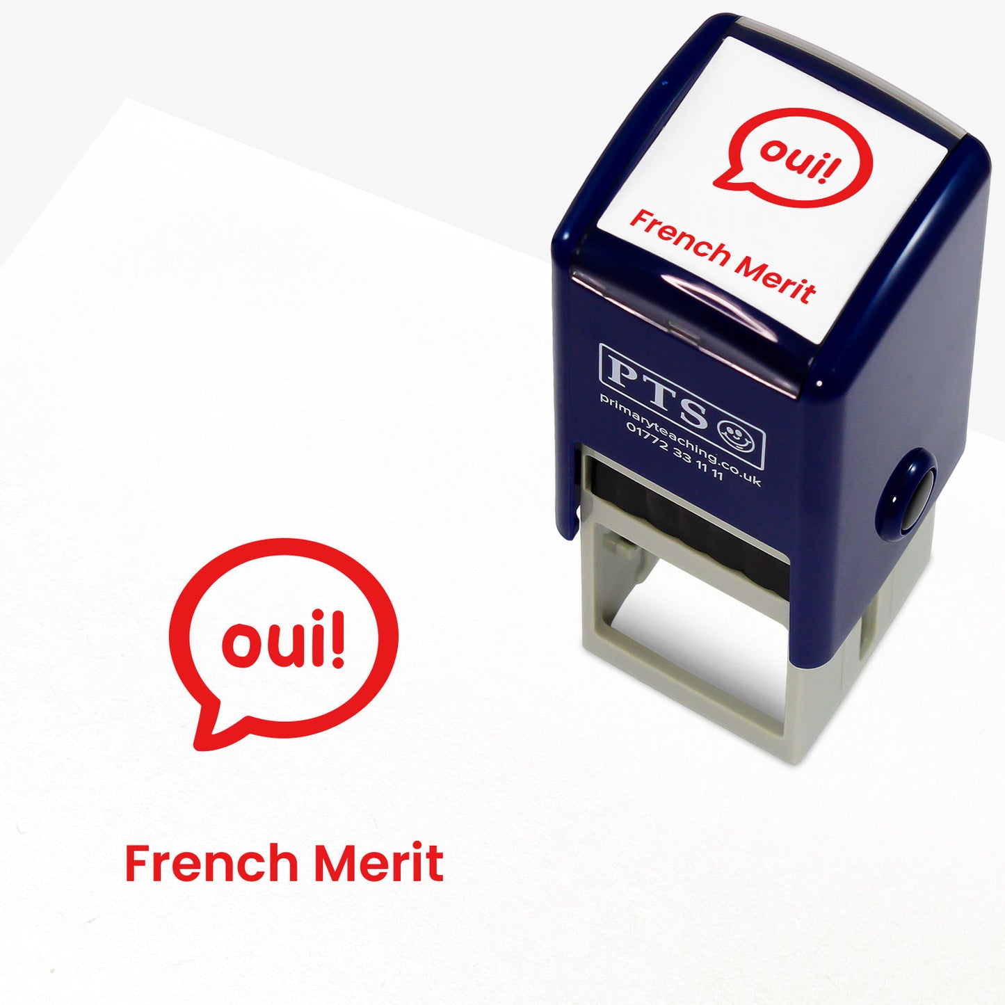 A stamper shown next to a sample stamped image on a white background. The stamp has a red outline of the word 'oui!' inside a shield shape, with placeholder text 'French Merit' on the top panel and below the stamp print.