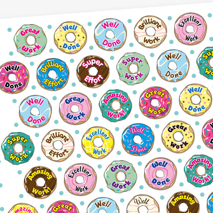 Sheet of 32mm vanilla-scented doughnut stickers in assorted pastel colours, each featuring phrases like 'Well Done', 'Great Work', and 'Brilliant Effort' in bold fonts; designed for rewarding pupils' achievements.