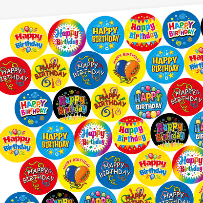 Sheet of strawberry scented round birthday stickers in various bright colours and designs. Each sticker features the phrase 'Happy Birthday' in different playful fonts, with decorative elements such as balloons, stars, swirls, and confetti. Backgrounds include red, yellow, rainbow, blue, and black themes.
