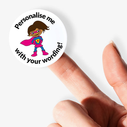Circular sticker with superhero design and text 'Personalise me with your wording!' held between fingers.