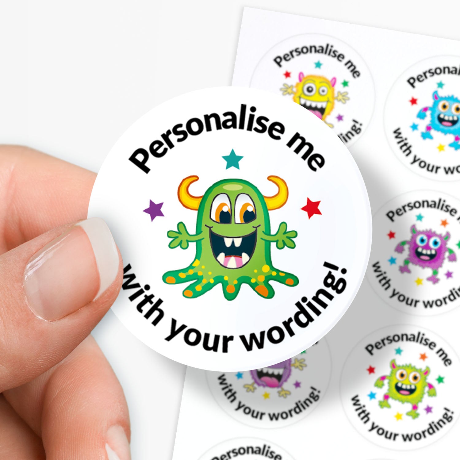 Circular sticker with a green monster graphic and text 'Personalise me with your wording!' held in between fingers.