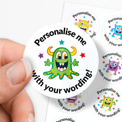 Circular sticker with a green monster graphic and text 'Personalise me with your wording!' held in between fingers.