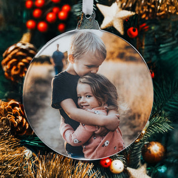 Round photo ornament with two children hugging, hanging on a Christmas tree.