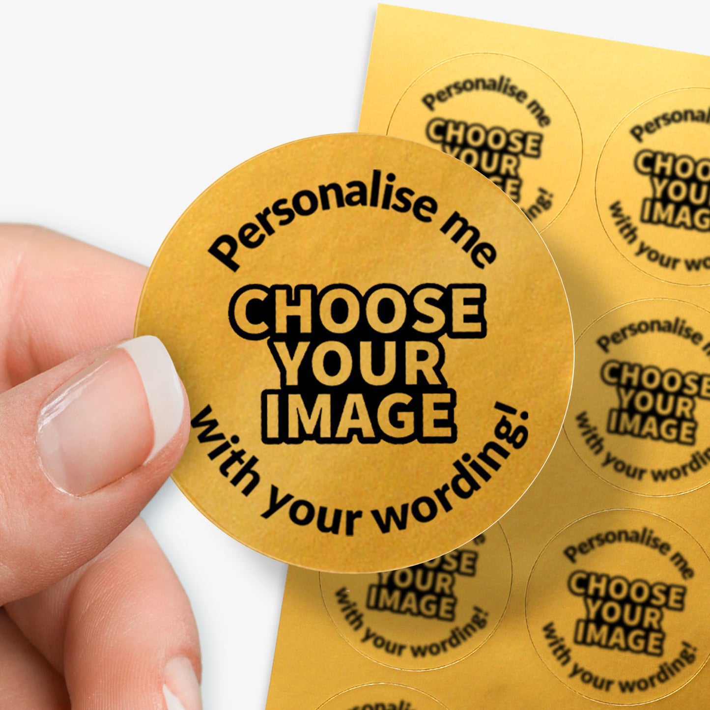 Round gold sticker with text 'Personalise me, choose your image with your wording!' held between fingers with sheet in the background.