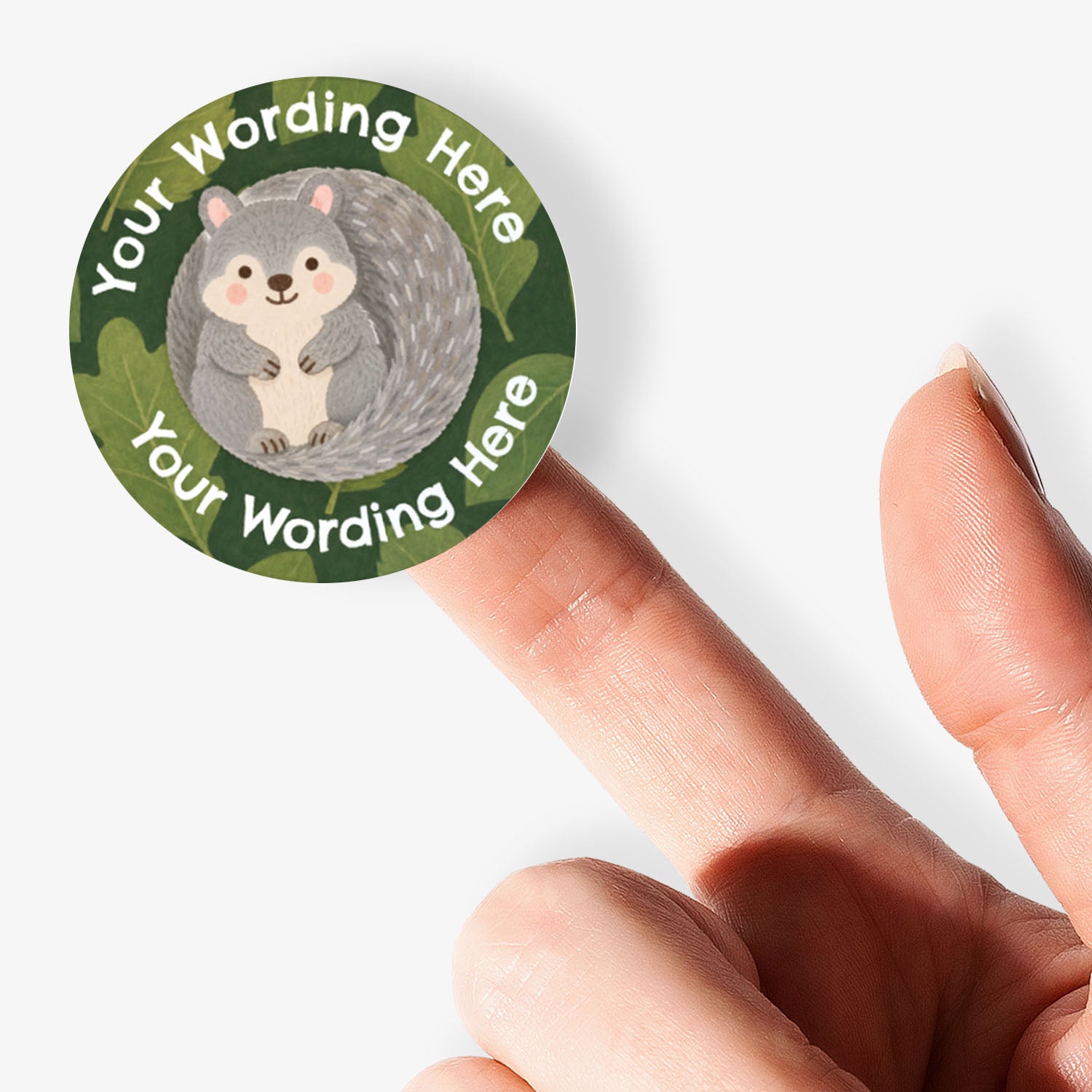 A close-up of a person's finger holding a circular custom sticker featuring a grey squirrel on a green leafy background with placeholder text 'Your Wording Here'.