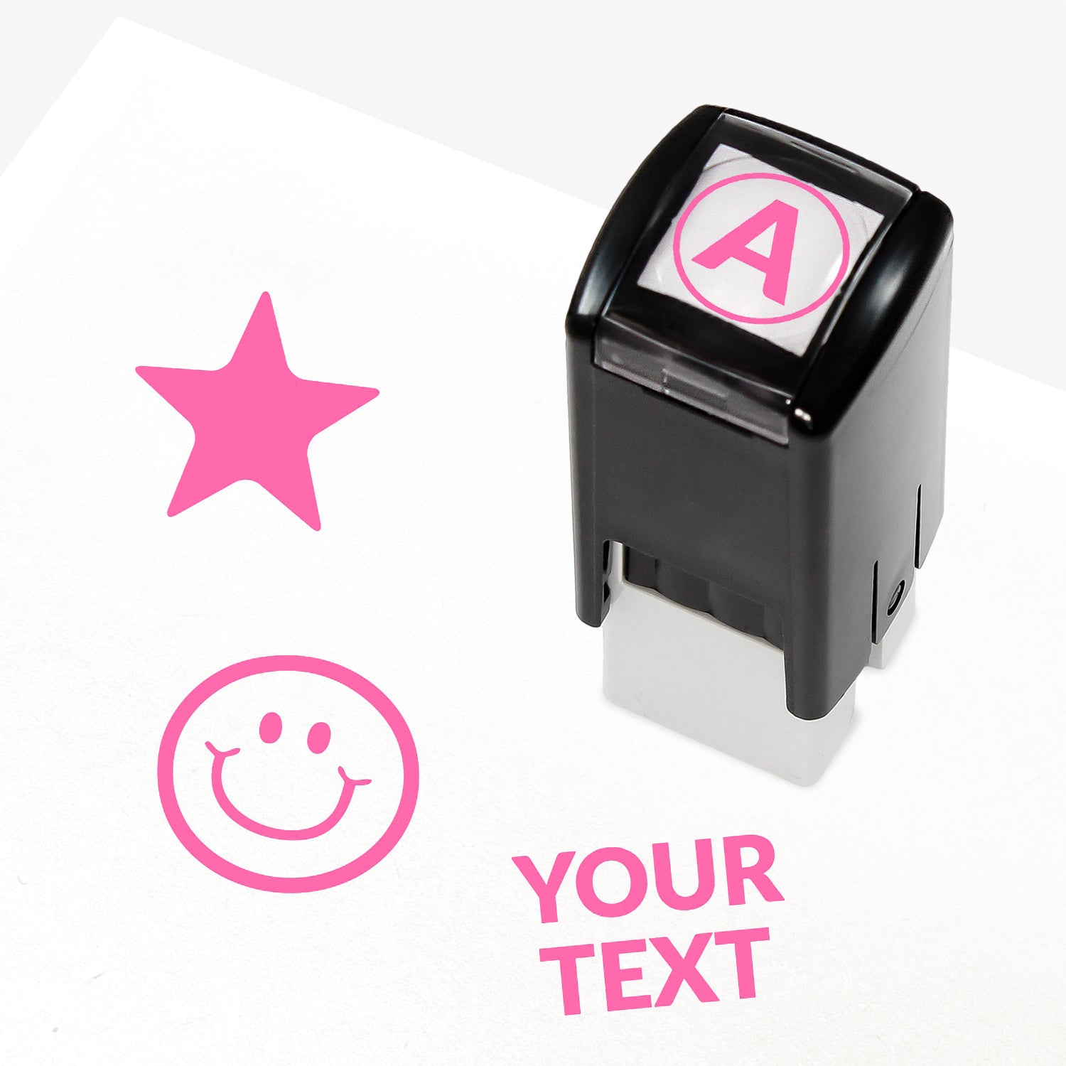 Customisable pink self-inking 10mm stamper with the placeholder text 'YOUR TEXT' in bold pink, alongside alternative options for icons such as smiling face or star, indicating space for a personalised image or message.