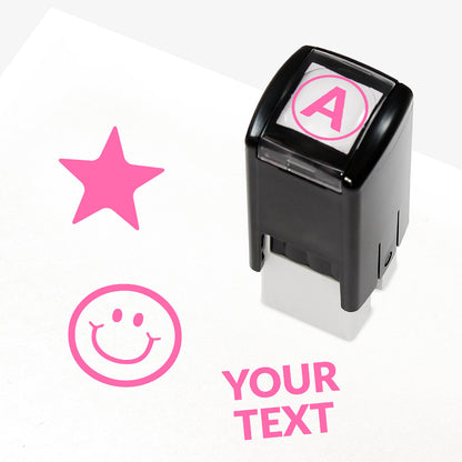 Customisable pink self-inking 10mm stamper with the placeholder text 'YOUR TEXT' in bold pink, alongside alternative options for icons such as smiling face or star, indicating space for a personalised image or message.