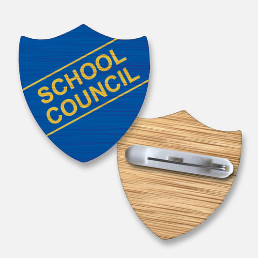 Eco-friendly bamboo shield-shaped badge measuring 34mm x 36mm, featuring a blue background with 'SCHOOL COUNCIL' inscribed diagonally in bold yellow lettering. The badge showcases a natural wood grain finish and includes a pin fastening on the reverse for secure attachment.