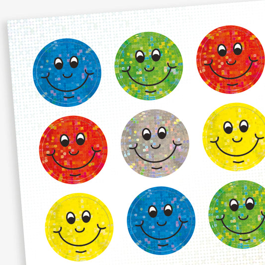 A sheet of colourful circular smiley face stickers with a holographic finish. Each sticker features a cheerful smiling face in different colours including blue, green, red, silver, and yellow.