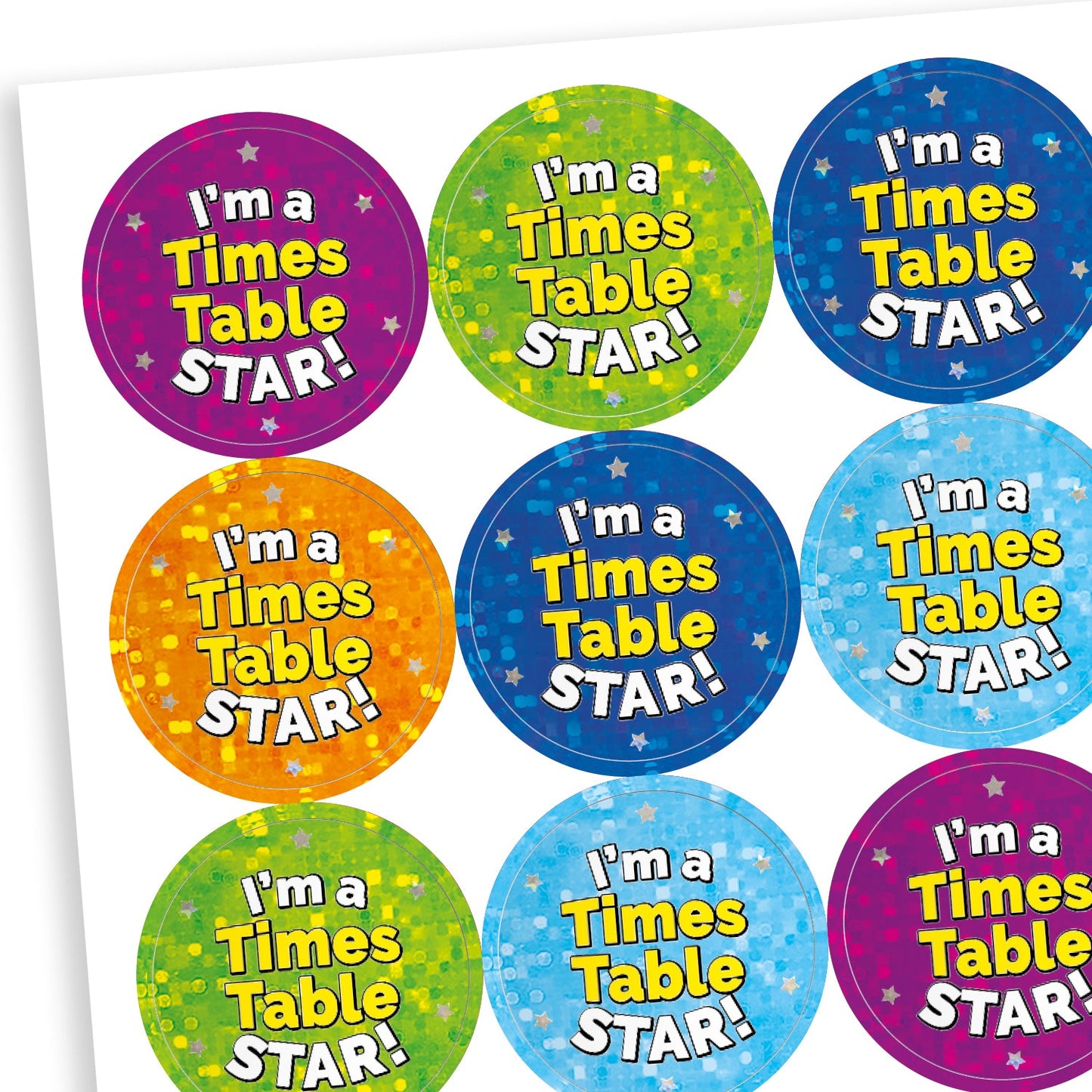 A sheet of round holographic reward stickers with the phrase 'I'm a Times Table STAR!' in bold white and yellow text. The stickers have starry backgrounds in various bright colours including blue, red, green, purple, and turquoise, creating a cheerful and encouraging appearance.