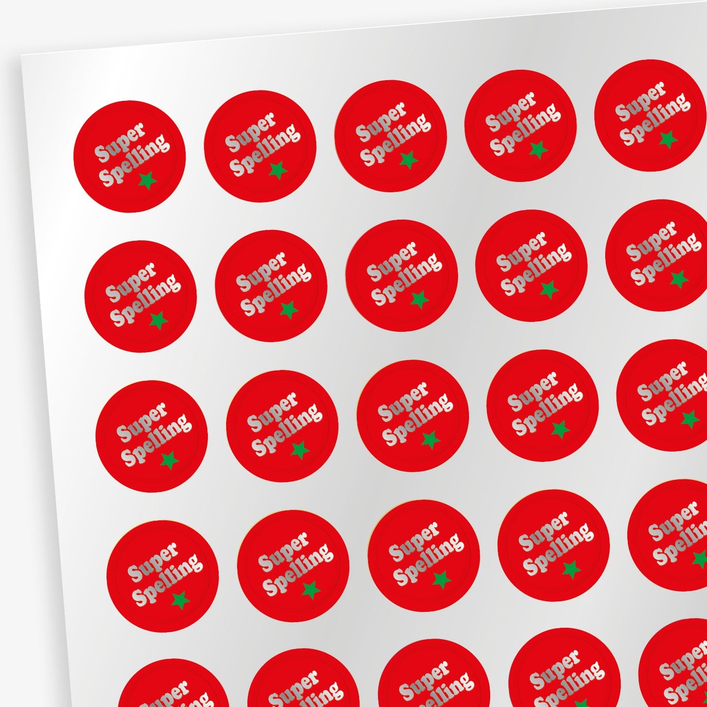 Sheet of 196 metallic 10mm circular reward stickers with a red background, each featuring the phrase 'Super Spelling' in bold silver lettering with a green star beneath. The stickers have a shiny, reflective finish and are designed to motivate and reward pupils' achievements.