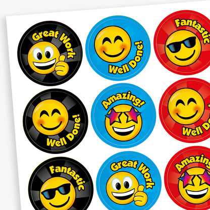 A sheet of colourful reward stickers featuring cheerful smiley faces with different expressions. Each circular sticker includes praise such as 'Great Work', 'Well Done!', 'Fantastic', and 'Amazing!'. The backgrounds are in bright colours like black, blue, and red, with each smiley wearing accessories like sunglasses or stars, designed to celebrate effort and achievement.