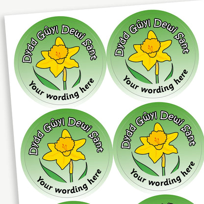 A sheet of green stickers featuring a daffodil in the centre.  Wording 'Dydd Gwyl Dewi Sant' is above the image. Placeholder text 'Your wording here' is below the image for customisation.