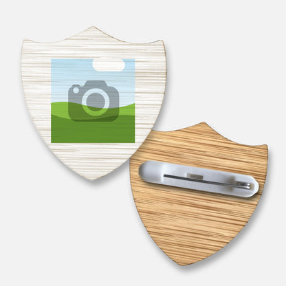 Front and back view of a customisable shield-shaped bamboo badge . The front displays a square image placeholder for personalisation, while the reverse features a metal safety pin fastening attached to the wood-textured surface.