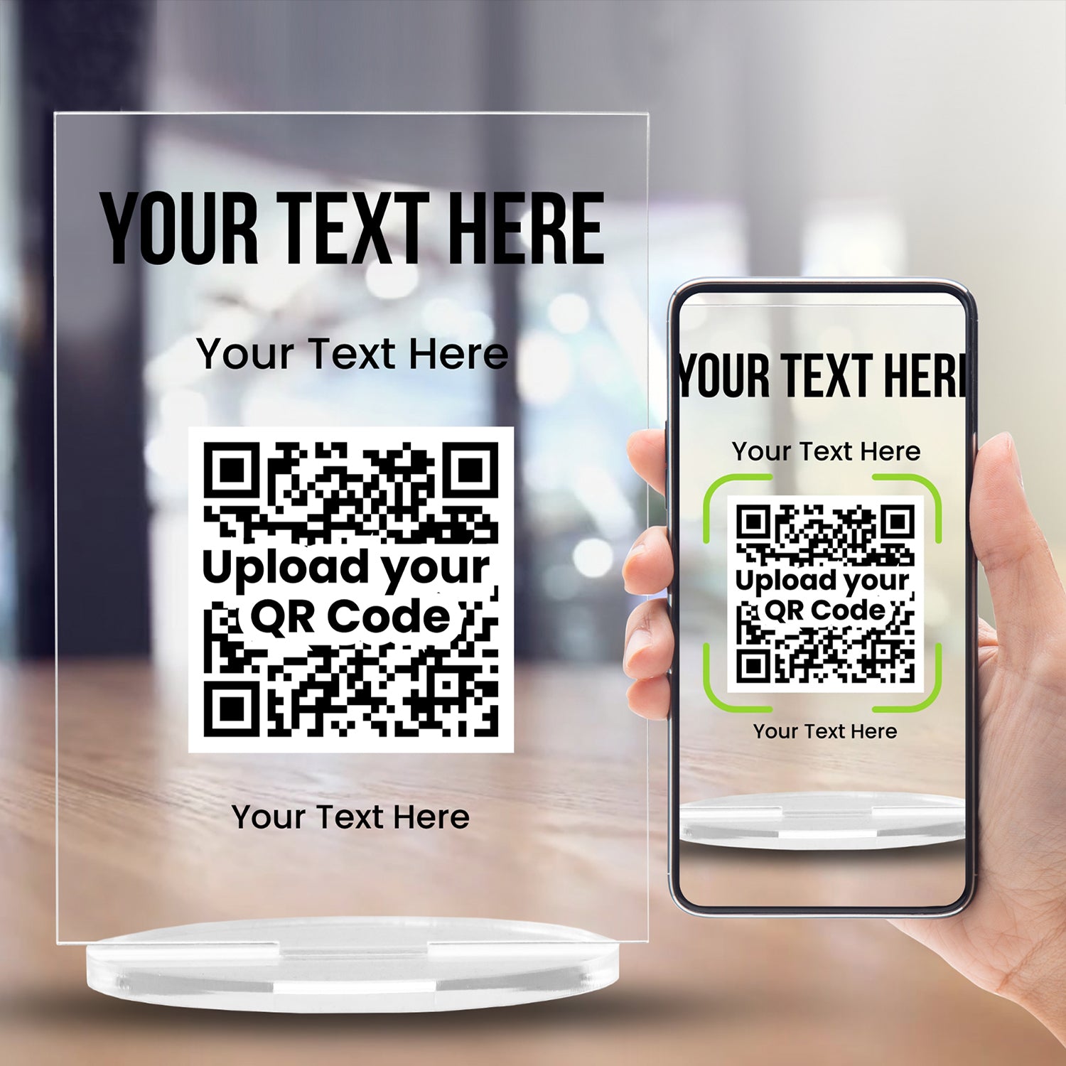 A clear acrylic sign with bold black text at the top reading 'YOUR TEXT HERE'. Below, it another placeholder 'Your Text Here'. A large black and white QR code is centrally displayed, and the placeholder 'Your Text Here' appears at the bottom. The sign stands upright on a circular clear base.  There ius a hand holding a mobile phone next to the plaque for scanning the QR code.