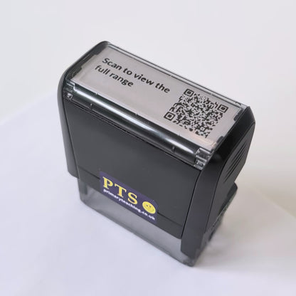 Custom QR code self-inking stamp shown stamping the text “Scan to view the full range” onto white paper.