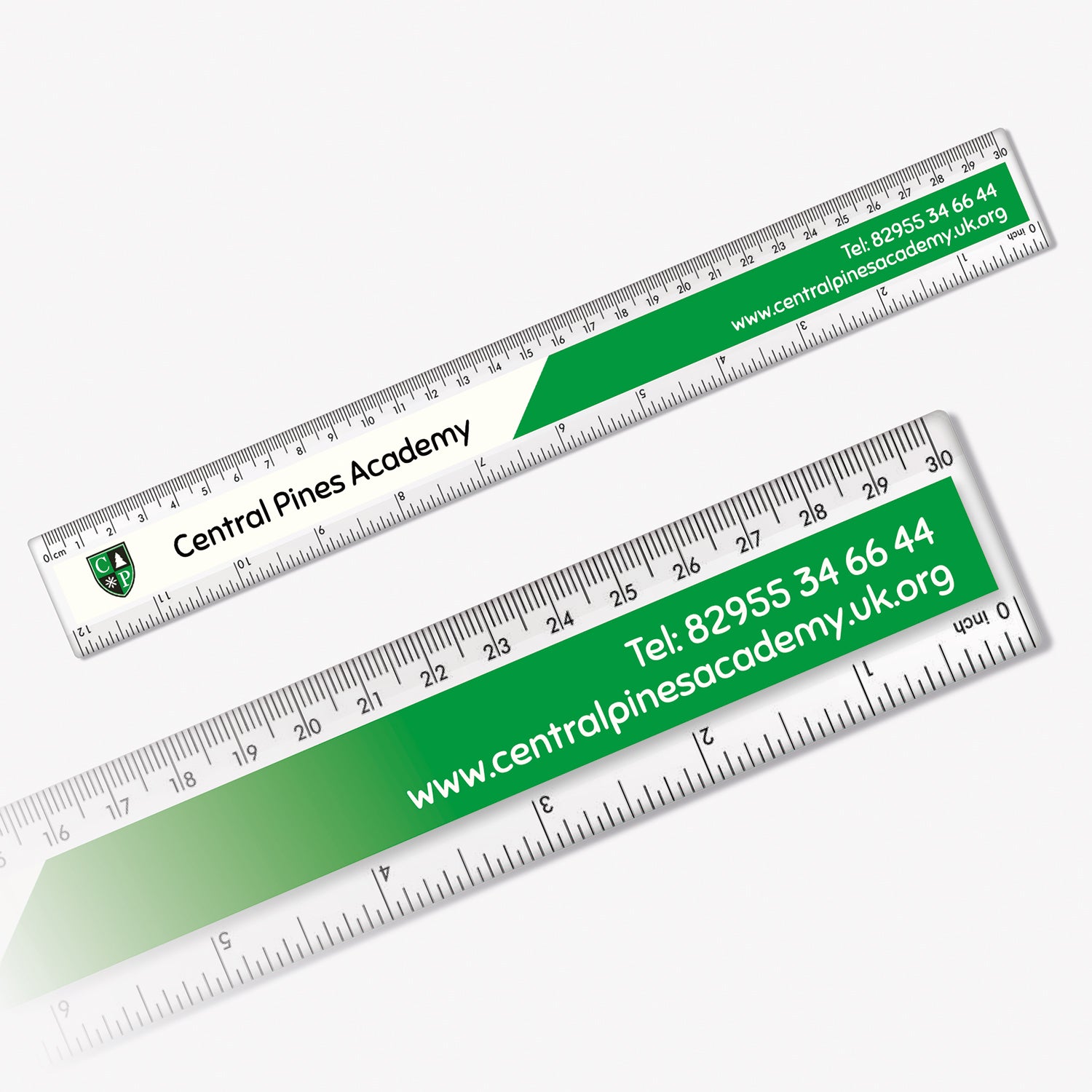 Two clear plastic rulers branded with 'Central Pines Academy'. One ruler features the school crest, name, telephone number, and website in white and green design. Measurement markings in centimetres and millimetres run along the top and inches along the bottom edges of both rulers.