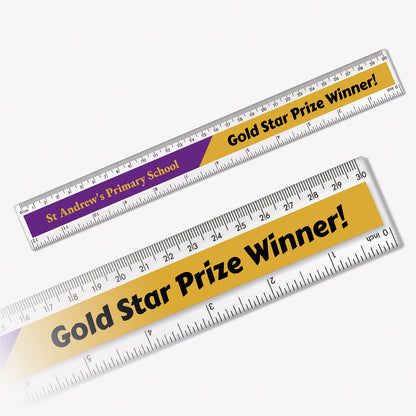 Twotone clear plastic rulers branded with 'St Andrew's Primary School' in gold font against a purple background with the other half of the ruler saying 'Gold Star Prize Winner!' in black font on a gold background. . Measurement markings in centimetres and millimetres run along the top and inches along the bottom edges of both rulers.