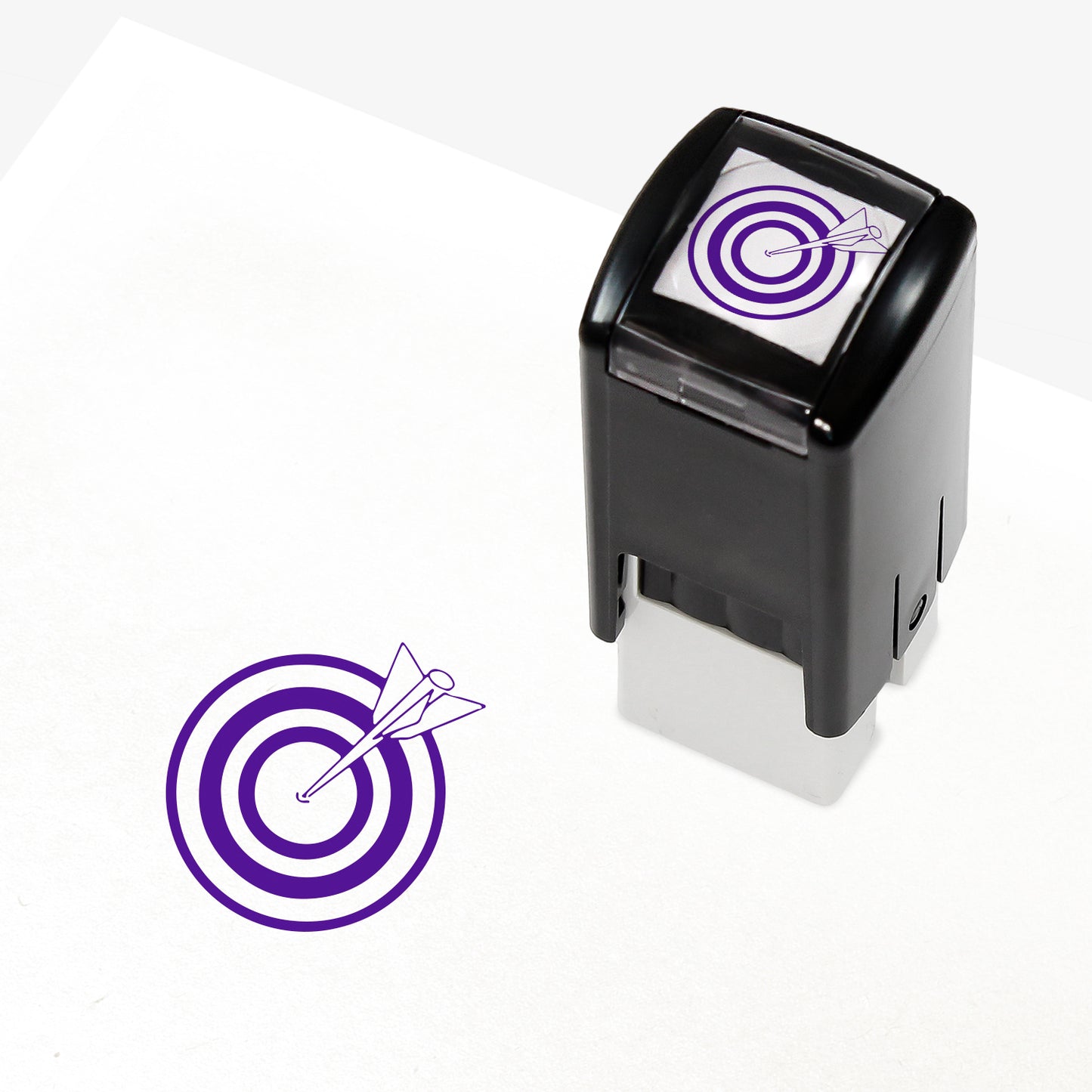 Target Stamper featuring a compact black casing with a purple bullseye and arrow design. The stamp imprint measures 10mm in diameter and is available in various ink colours, ideal for marking pupil achievements.