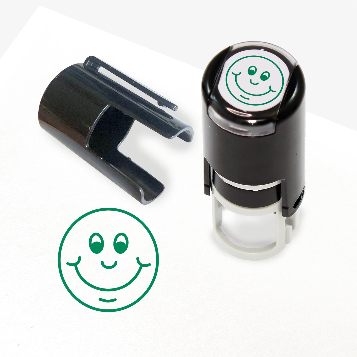 A 10mm self-inking stamp with a green outline of a smiling face central to the design.  The stamper lid also shows a clip for attaching the stamper to a lanyard.