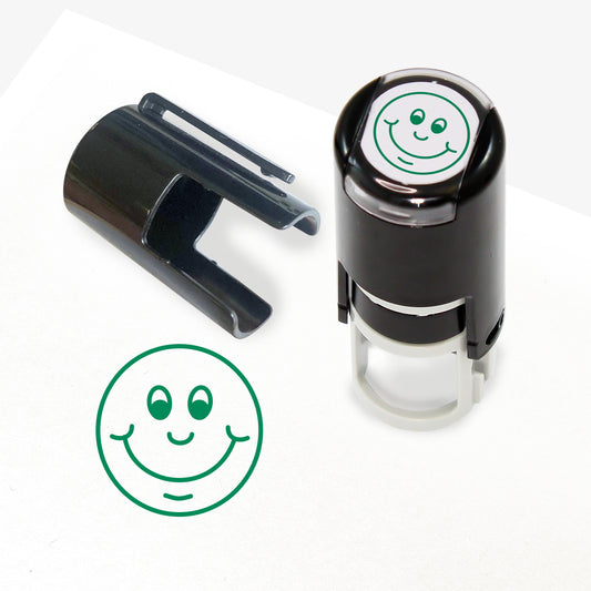 A 10mm self-inking stamp with a green outline of a smiling face central to the design.  The stamper lid also shows a clip for attaching the stamper to a lanyard.