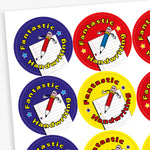 A sheet of circular reward stickers for children, each with a colourful background and the phrase 'Fantastic Handwriting'. Each sticker features a smiling cartoon pencil with arms and legs, positioned over a sheet of lined paper. The backgrounds are in different colours: blue, red, yellow, and purple.