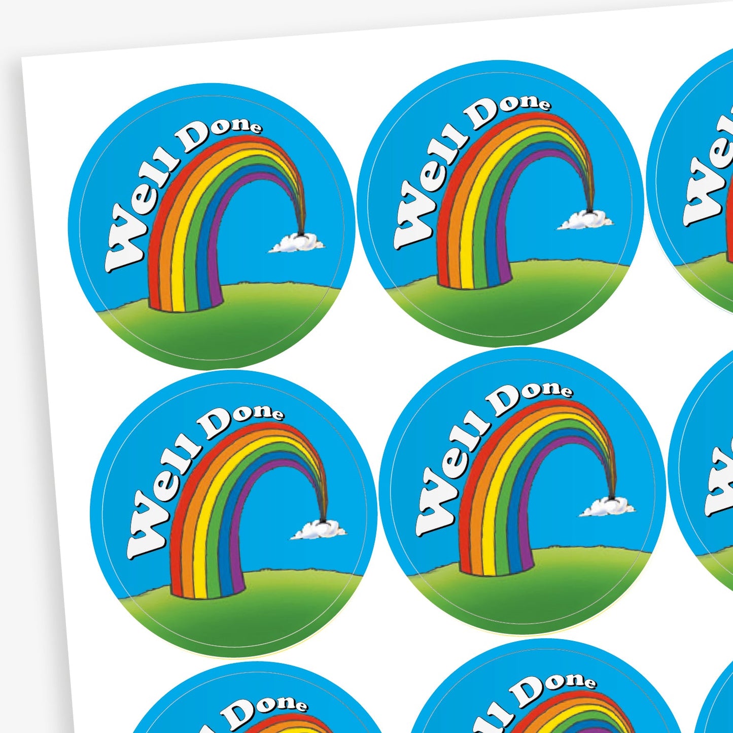 Sheet of round reward stickers featuring a rainbow arching over a green hill with the words 'Well Done' in white on a blue sky background with small clouds.