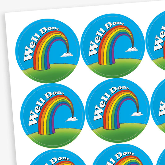 Sheet of round reward stickers featuring a rainbow arching over a green hill with the words 'Well Done' in white on a blue sky background with small clouds.
