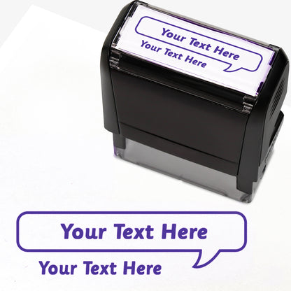 Rectangular self-inking stamper measuring 59mm by 21mm, featuring the phrase 'Your Text Here' leading onto a speech bubble going above it also saying 'Your Text Here'. In purple ink.