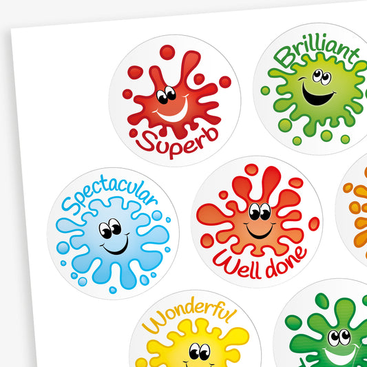 A sheet of round, jellybean scented reward stickers, each featuring a colourful paint splat character with a smiling face. The stickers include positive words in playful fonts, such as 'Superb' on a red splat, 'Brilliant' on a green splat, 'Tremendous' on a darker green splat, and 'Magnificent' on a purple splat. Each design is vibrant and visually engaging.