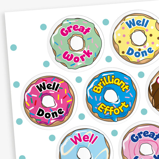 Sheet of 32mm vanilla-scented doughnut stickers in assorted pastel colours, each featuring phrases like 'Well Done', 'Great Work', and 'Brilliant Effort' in bold fonts; designed for rewarding pupils' achievements.