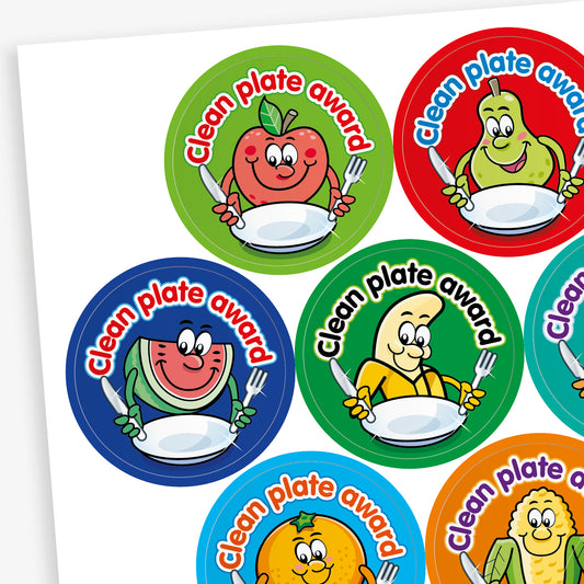 A fruity scented sheet of colourful circular 'Clean Plate Award' stickers featuring smiling cartoon fruits and vegetables, such as an apple, pear, corn, and pineapple, each holding a knife and fork with an empty plate. Background colours include green, red, orange, and purple.