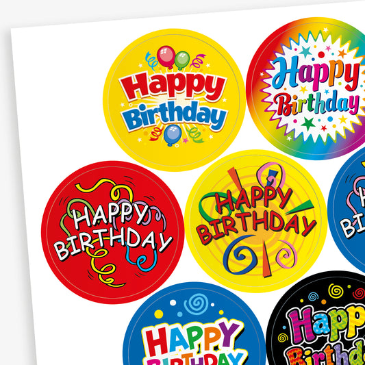 Sheet of strawberry scented round birthday stickers in various bright colours and designs. Each sticker features the phrase 'Happy Birthday' in different playful fonts, with decorative elements such as balloons, stars, swirls, and confetti. Backgrounds include red, yellow, rainbow, blue, and black themes.
