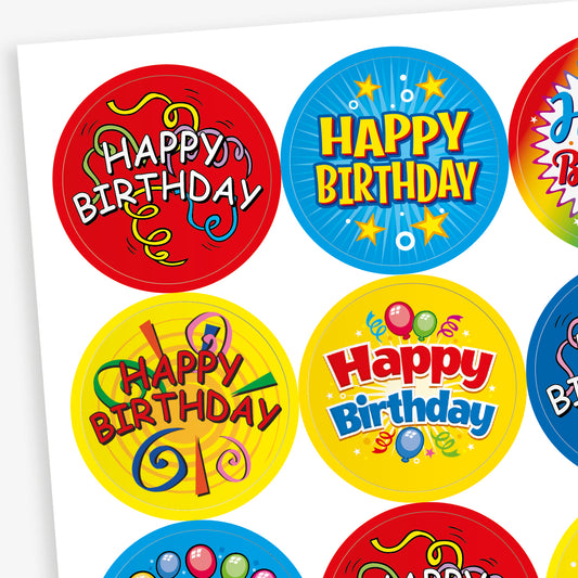 Sheet of strawberry scented round birthday stickers in various bright colours and designs. Each sticker features the phrase 'Happy Birthday' in different playful fonts, with decorative elements such as balloons, stars, swirls, and confetti. Backgrounds include red, yellow, rainbow, blue, and black themes.
