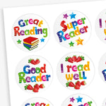 Sheet of strawberry scented round reward stickers with colourful text promoting reading achievements. Messages include 'Great Reading', 'Super Reader', 'Good Reader', and 'I read well', with accompanying illustrations of stars, strawberries, and a stack of books. Each sticker features vibrant, multicoloured lettering on a white background.